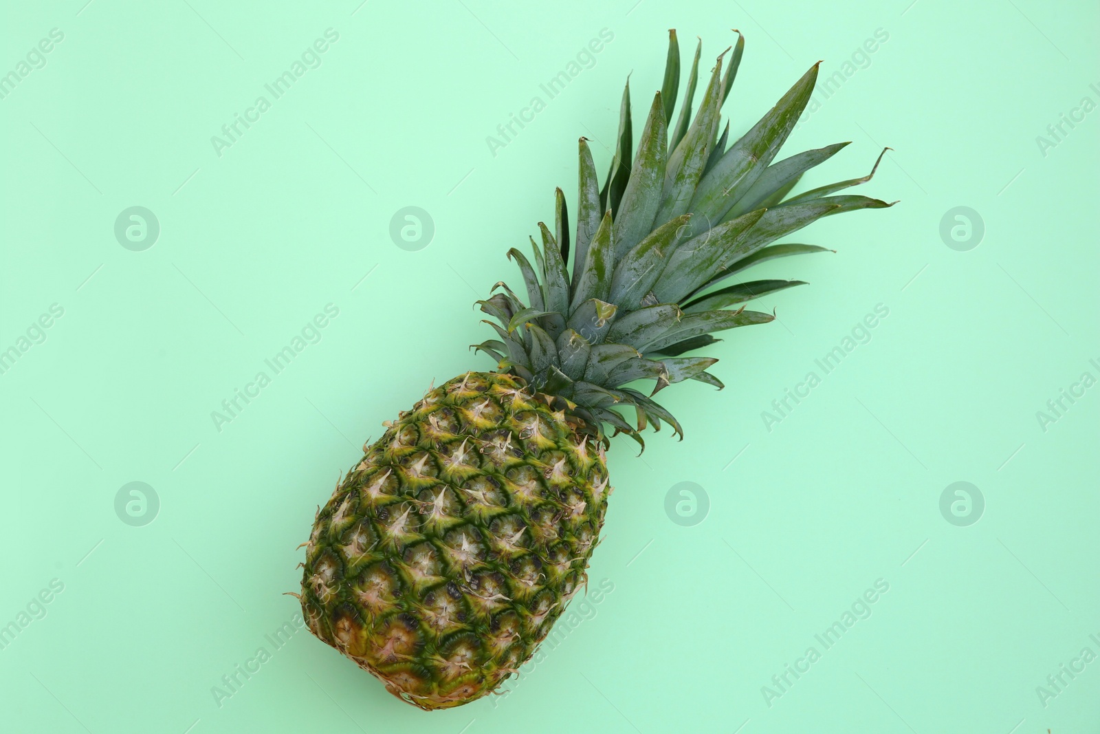 Photo of Whole ripe pineapple on light green background, top view