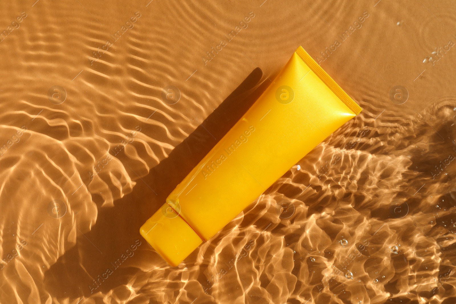 Photo of Tube with moisturizing cream in water on orange background, top view