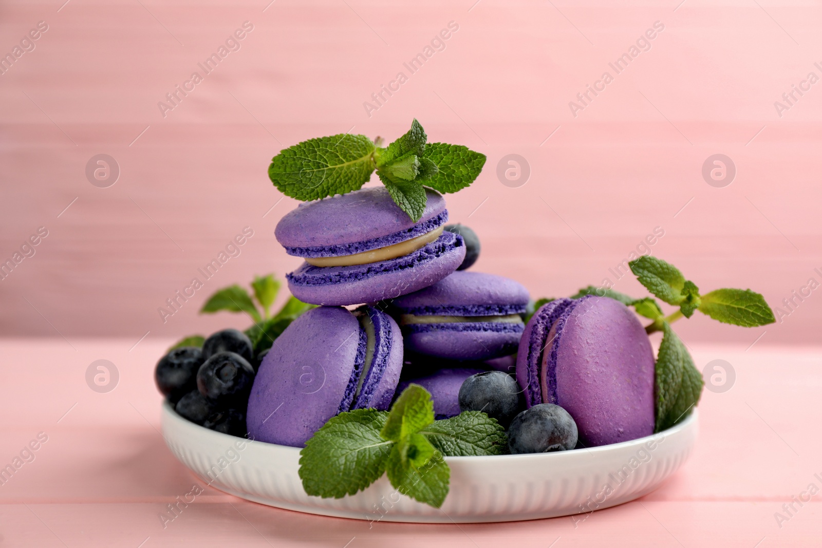 Photo of Delicious macarons, mint and blueberries on pink wooden table