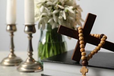 Photo of Wooden cross, rosary beads, Bible, church candles and flowers on light table, closeup