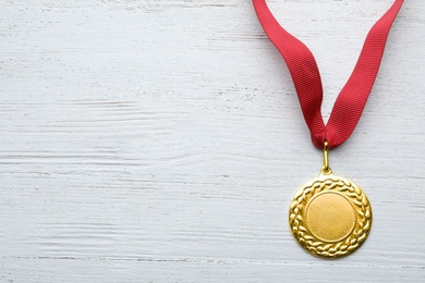 Photo of Gold medal with space for design on white wooden background, top view. Victory concept