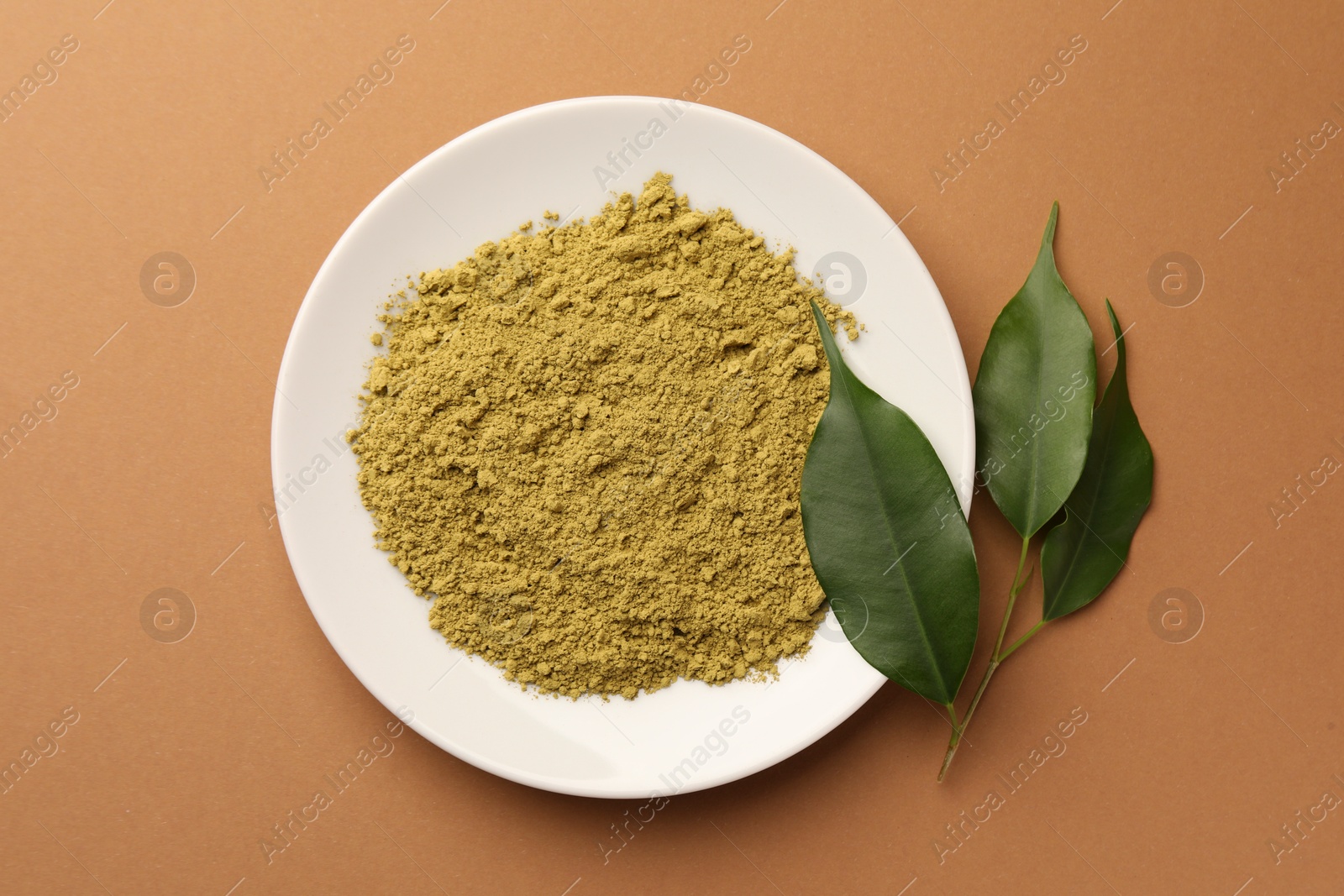 Photo of Henna powder and green leaves on coral background, flat lay. Natural hair coloring