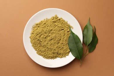 Henna powder and green leaves on coral background, flat lay. Natural hair coloring
