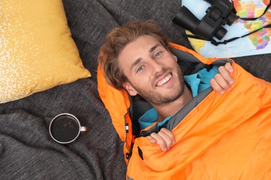 Young man in comfortable sleeping bag on blanket, top view