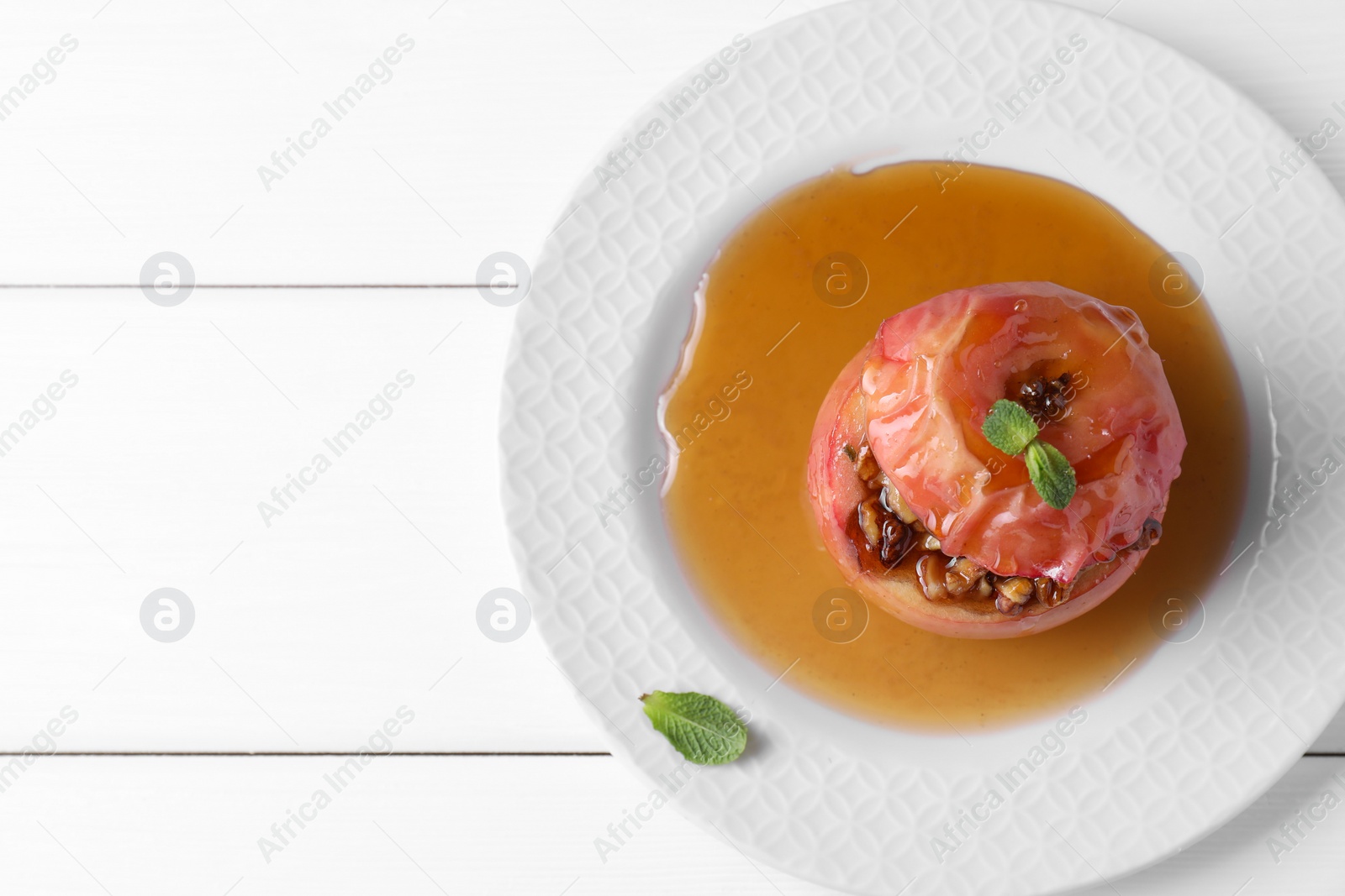 Photo of Tasty baked apple with nuts, honey and mint on white wooden table, top view. Space for text