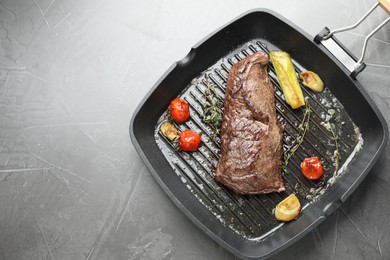 Delicious grilled beef meat and vegetables in pan on grey table, top view. Space for text