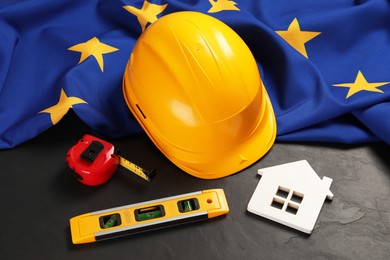 Photo of House model, construction tools and flag of European Union on black table