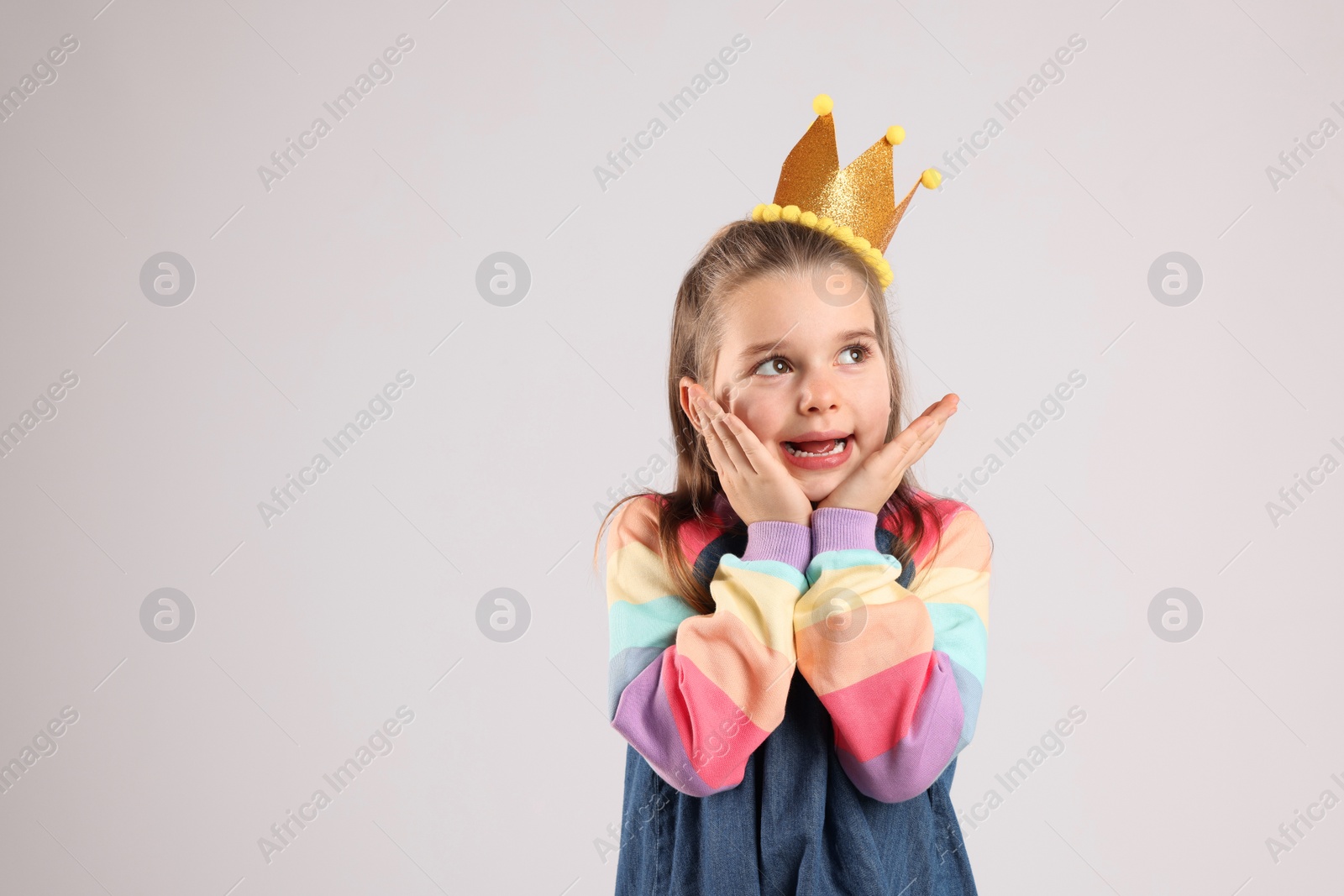 Photo of Cute girl in golden crown on light grey background, space for text. Little princess