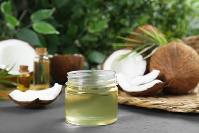 Jar of organic coconut cooking oil and fresh fruits on grey table, closeup