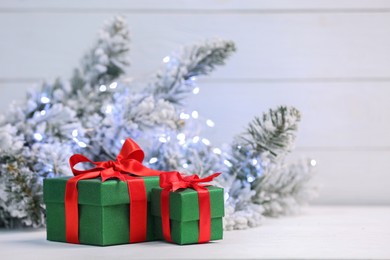 Photo of Beautiful gift boxes on white table against blurred festive lights, space for text. Christmas present