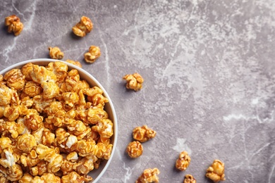Photo of Delicious popcorn with caramel in bowl on gray background, top view