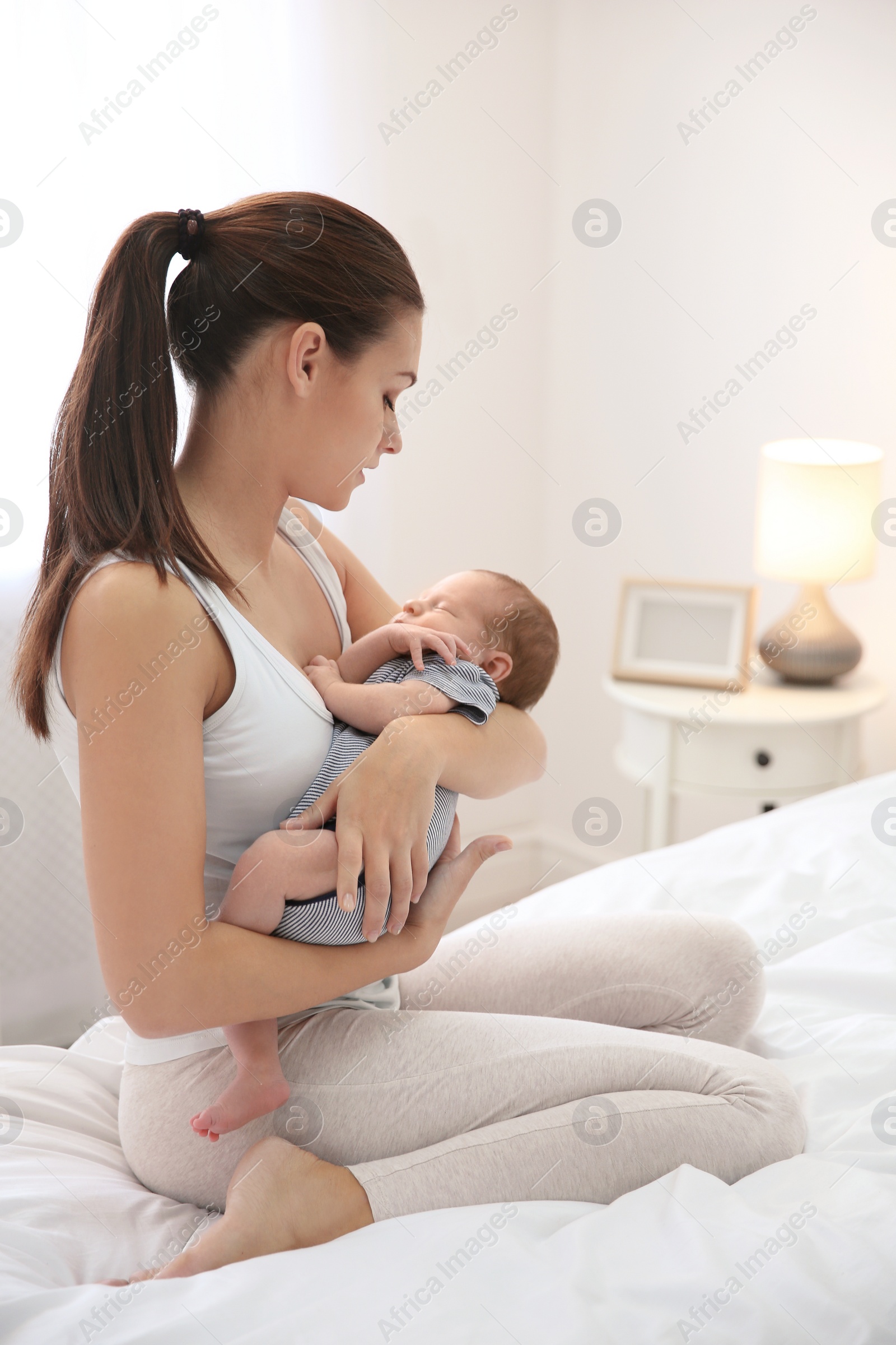 Photo of Young woman holding her baby near breast in bedroom