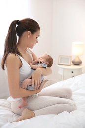 Young woman holding her baby near breast in bedroom