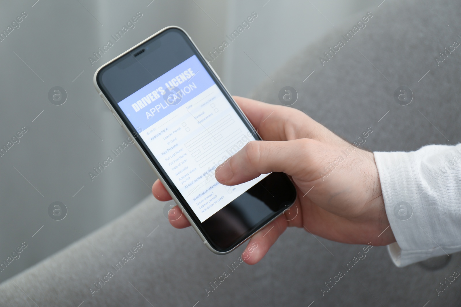 Photo of Man holding smartphone with driver's license application form at home, closeup