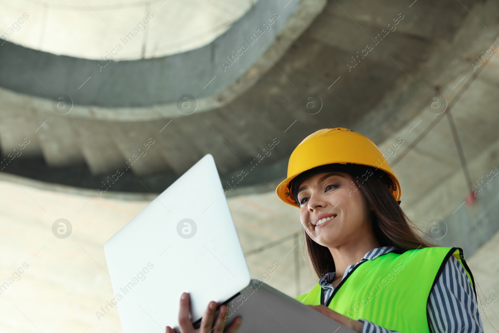 Photo of Professional engineer in safety equipment with laptop at construction site. Space for text