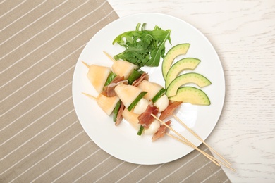 Photo of Plate with melon, mozzarella and prosciutto skewers on table, top view