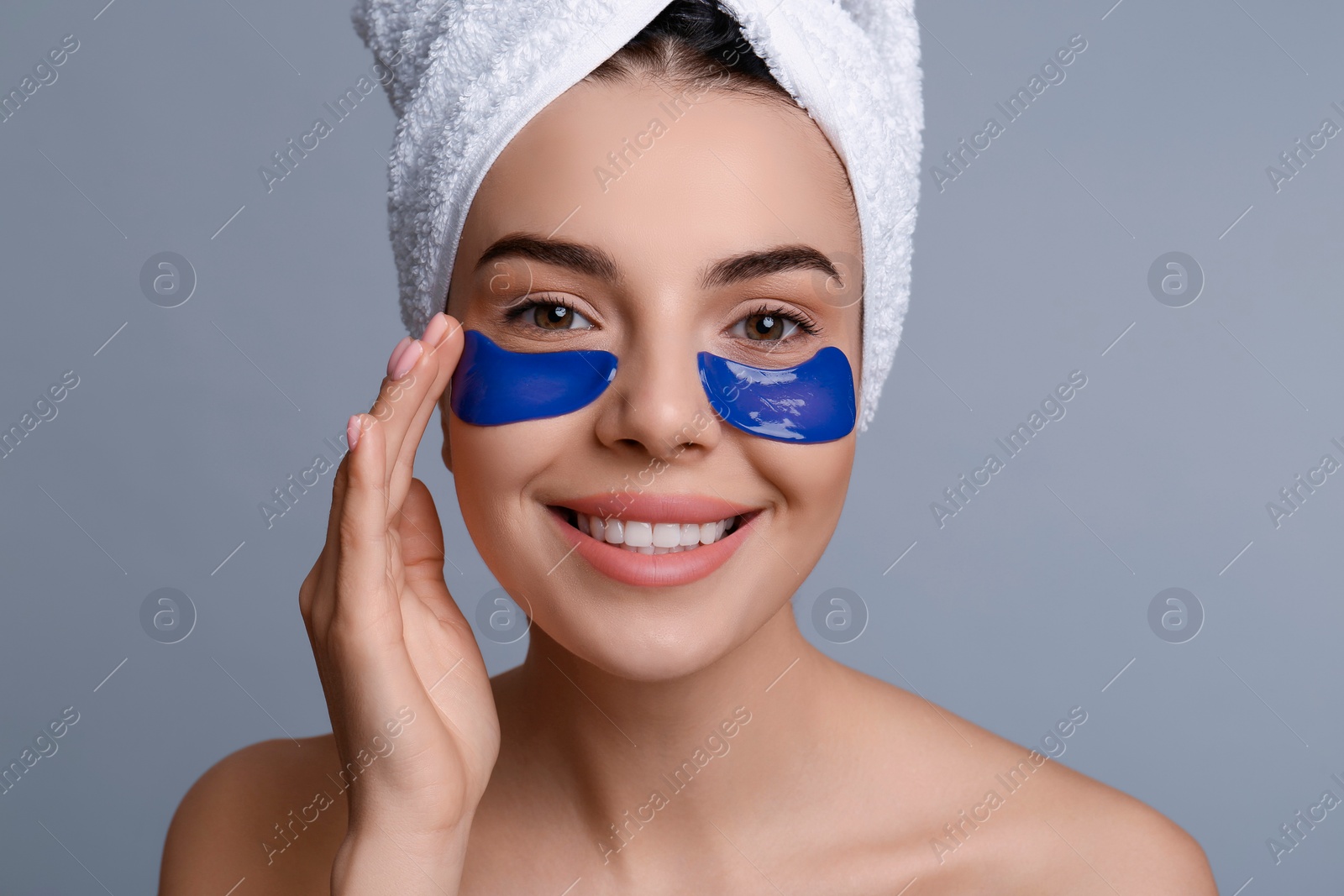 Photo of Beautiful young woman with under eye patches and hair wrapped in towel on grey background