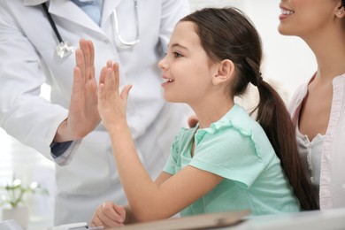 Photo of Mother with daughter visiting pediatrician in hospital. Doctor giving high five to little girl