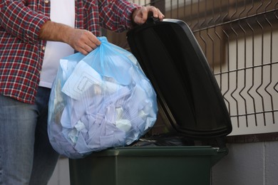 Man putting garbage bag into recycling bin outdoors, closeup