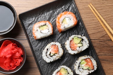 Delicious sushi rolls, soy sauce, ginger and chopsticks on wooden table, flat lay