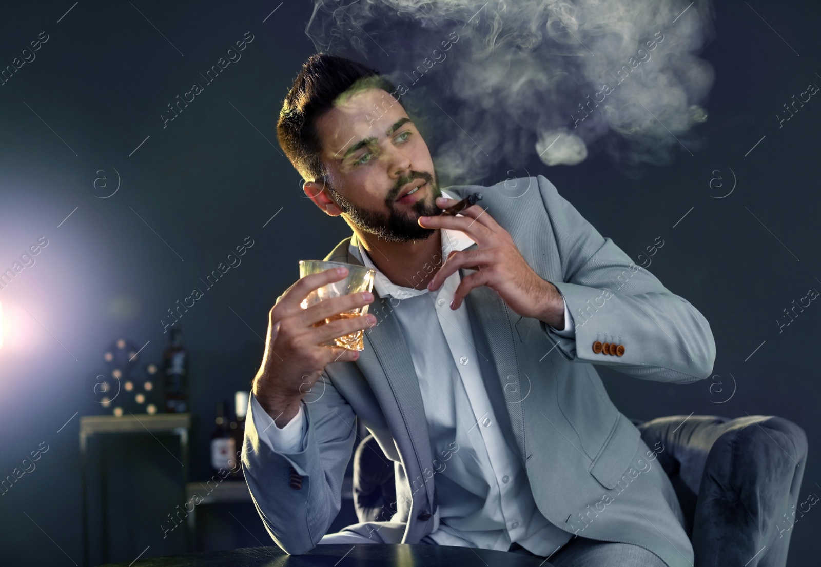 Photo of Man with glass of whiskey and cigar sitting at table indoors