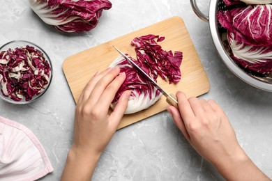 Photo of Woman cutting fresh ripe radicchio at light grey marble table, top view
