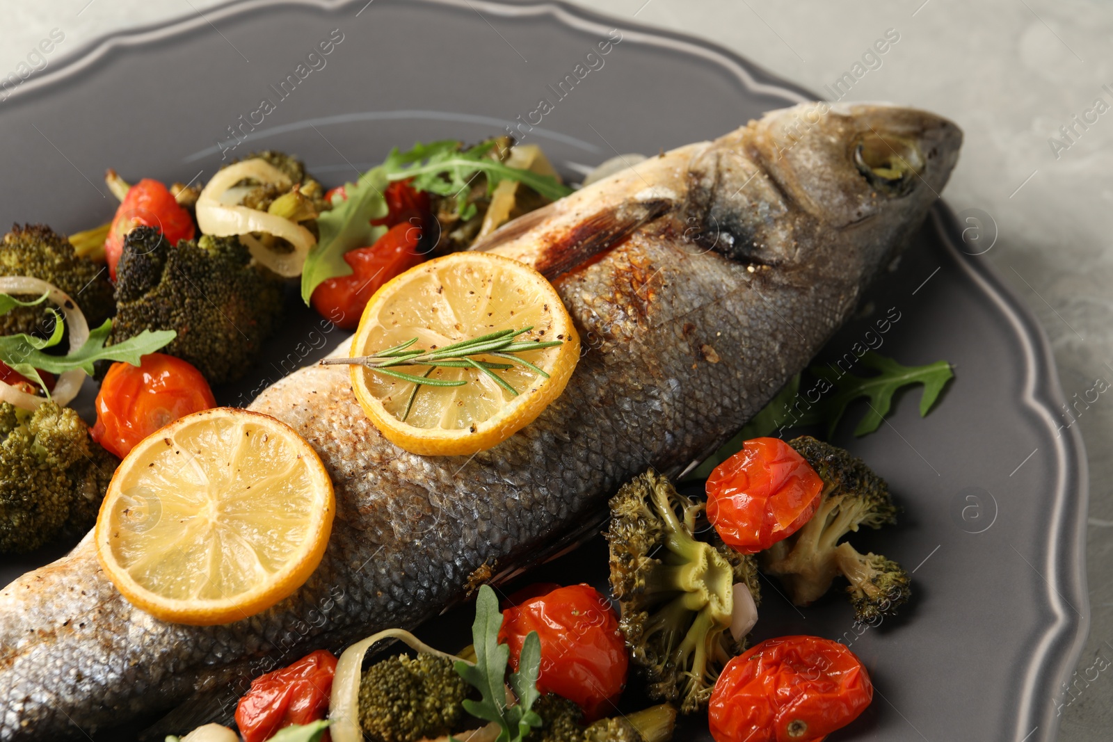 Photo of Baked fish with vegetables, rosemary and lemon on grey textured table, closeup