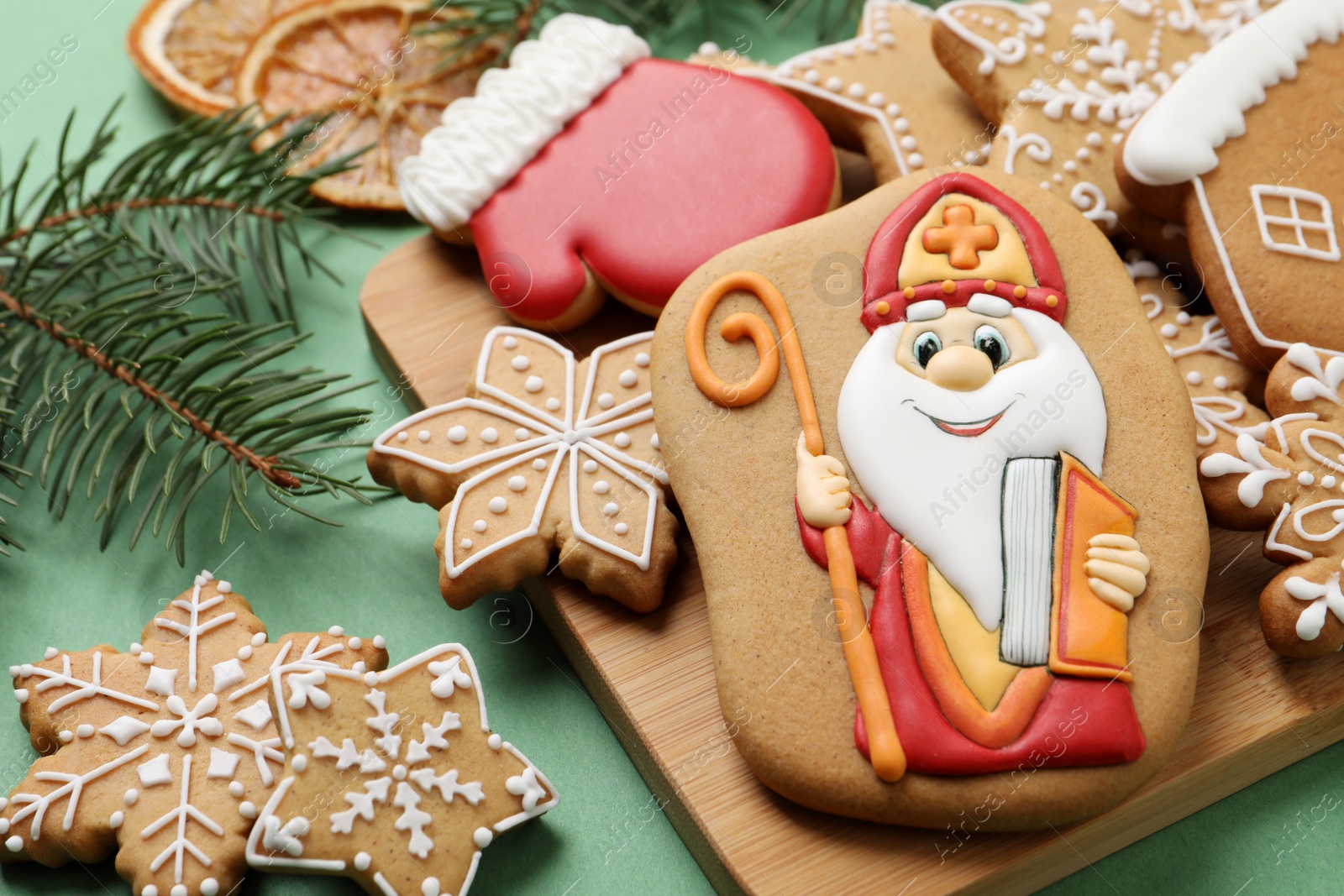 Photo of Tasty gingerbread cookies and fir branches on green background. St. Nicholas Day celebration
