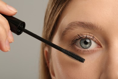 Photo of Woman applying mascara onto eyelashes against grey background, closeup