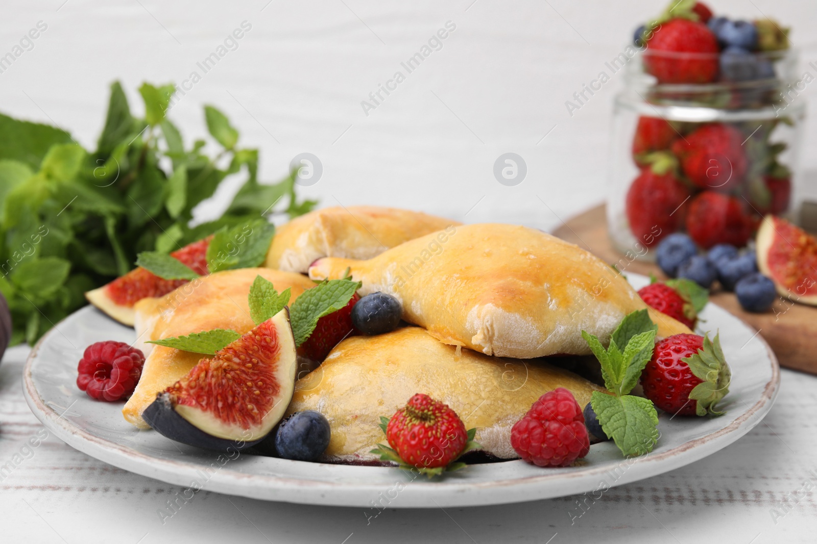 Photo of Delicious samosas with figs and berries on white wooden table, closeup