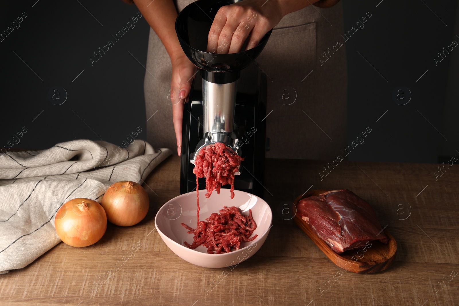 Photo of Woman making beef mince with electric meat grinder at wooden table, closeup