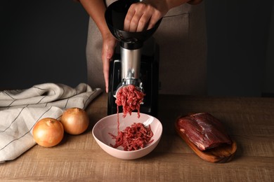 Woman making beef mince with electric meat grinder at wooden table, closeup