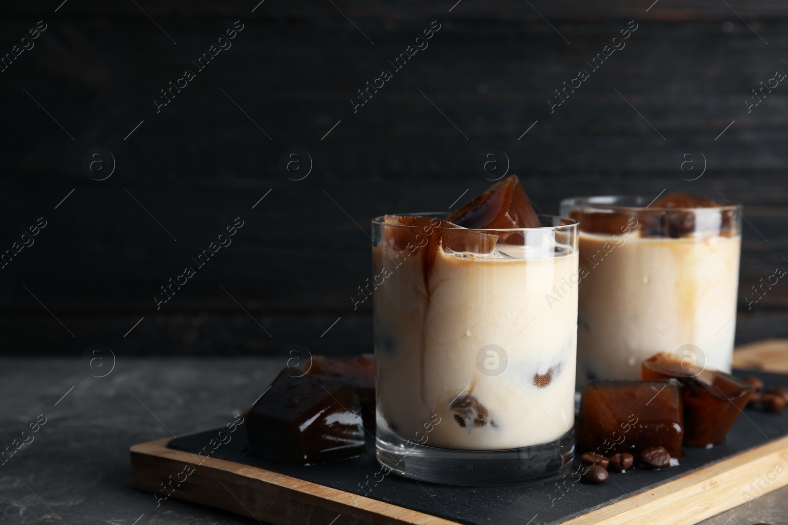 Photo of Glasses of milk with coffee ice cubes on table. Space for text