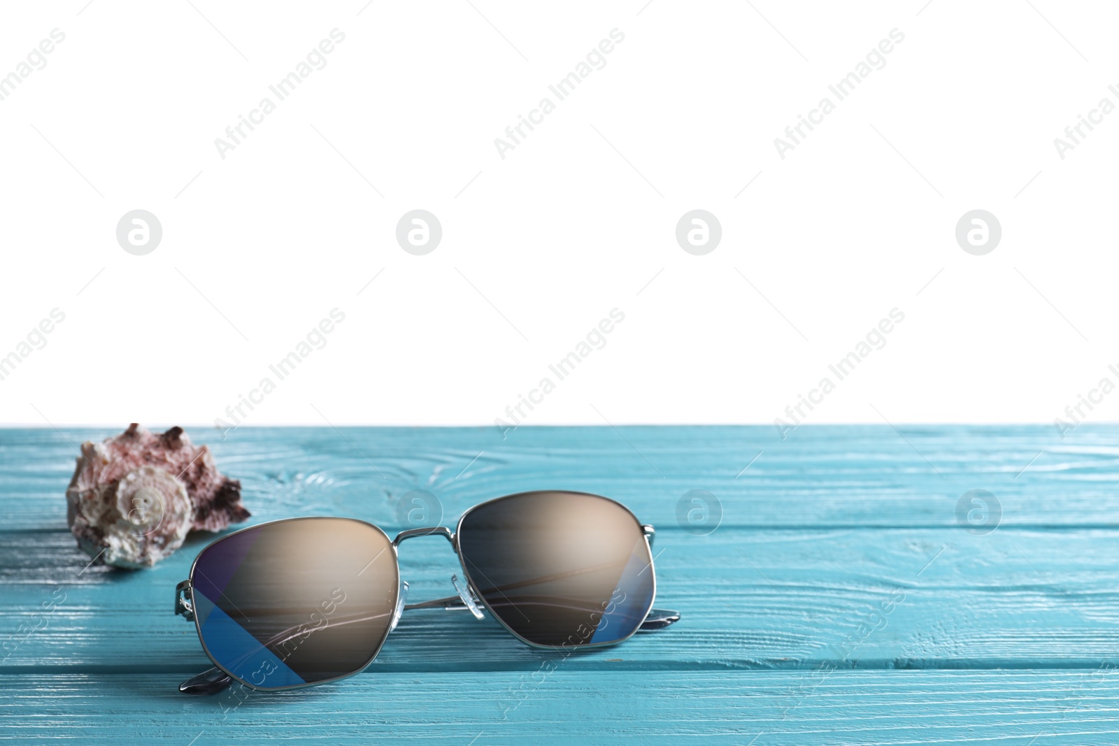 Photo of Stylish sunglasses and shell on light blue wooden table against white background. Space for text