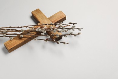 Photo of Wooden cross and willow branches on light grey background, space for text. Easter attributes