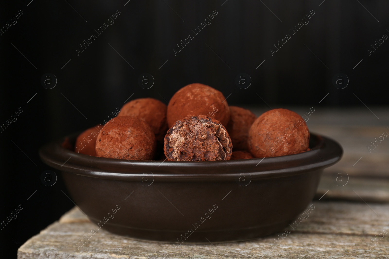 Photo of Delicious chocolate candies powdered with cocoa on wooden table, closeup