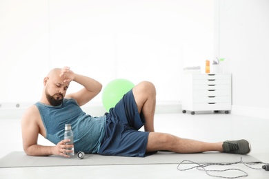 Photo of Tired overweight man with bottle of water in gym