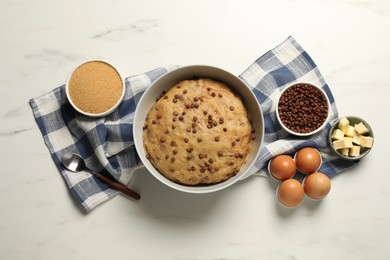 Photo of Bowl with dough and ingredients for cooking chocolate chip cookies on white marble table, flat lay