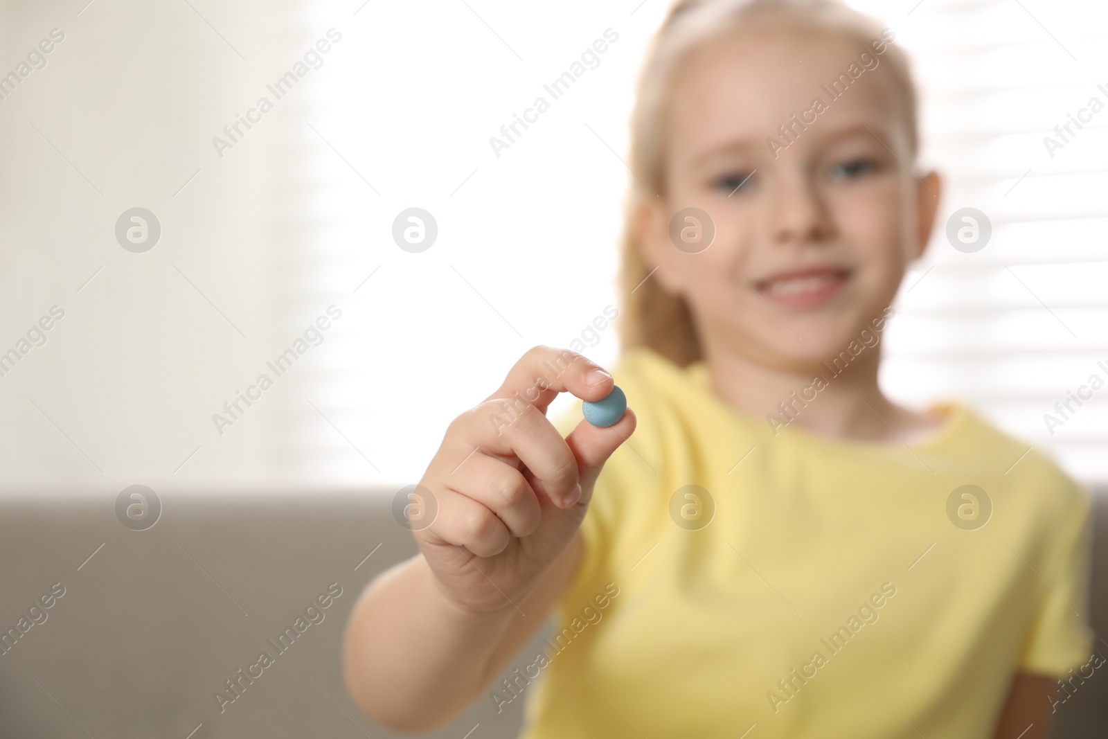 Photo of Little girl with vitamin pill at home, focus on hand