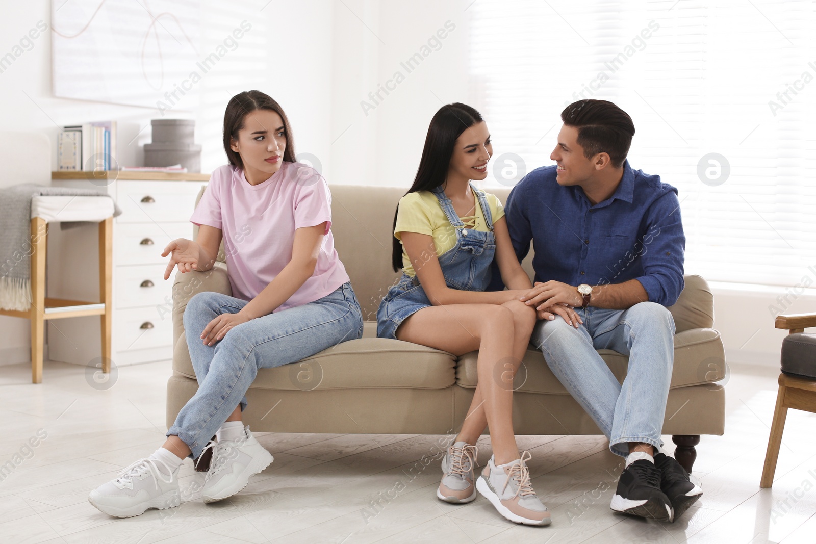 Photo of Unhappy woman feeling jealous while couple spending time together on sofa at home