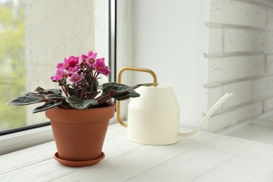 Beautiful potted violet flowers and watering can on white wooden window sill. Plant for house decor