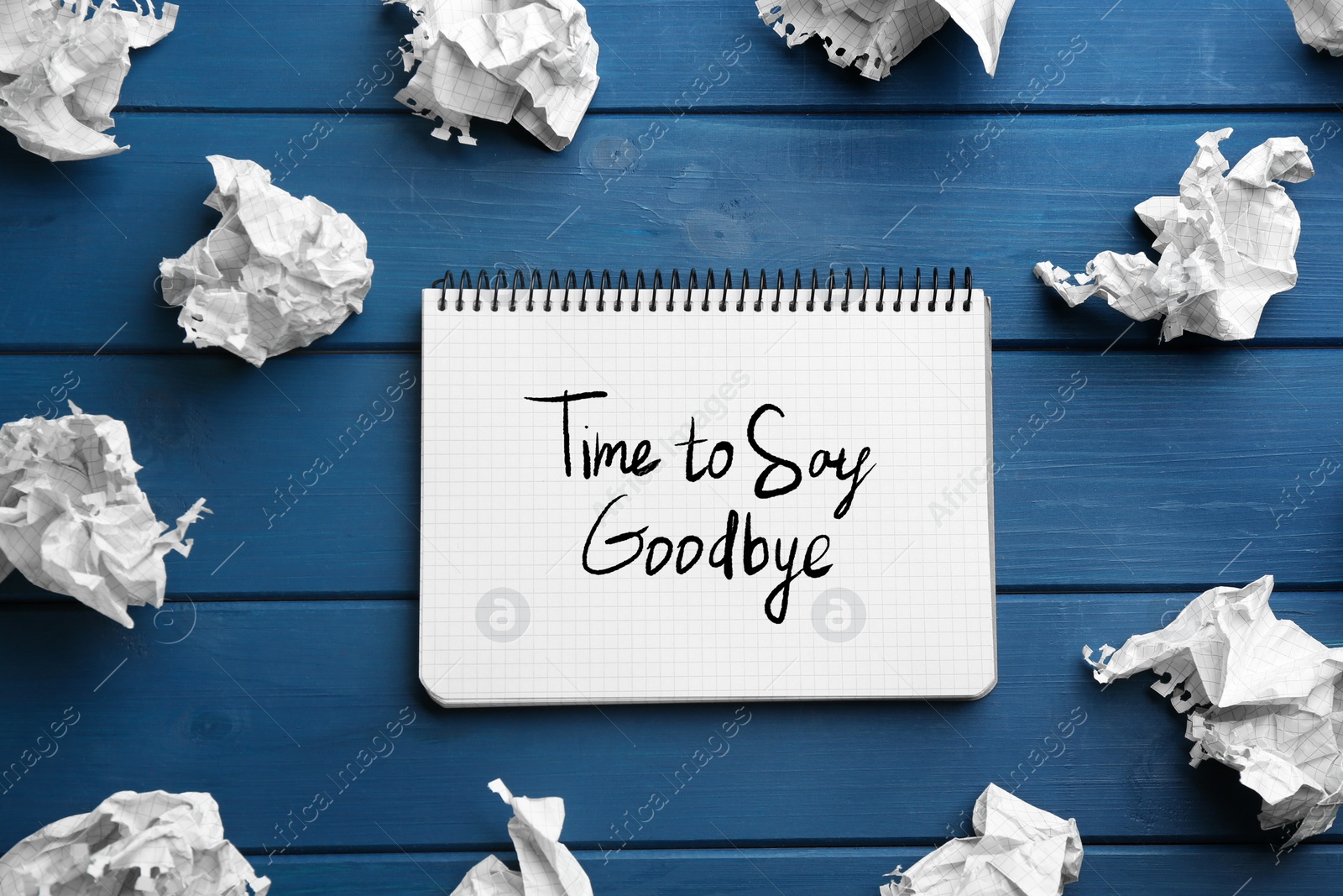 Image of Notebook with phrase Time to say Goodbye and crumpled sheets of paper on blue wooden background, flat lay