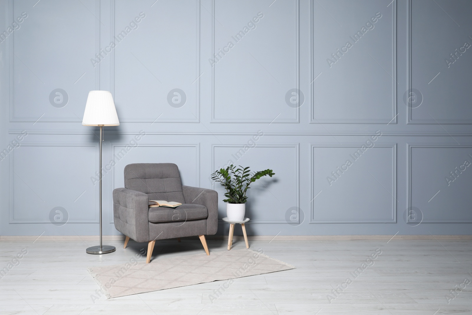 Photo of Cosy armchair, floor lamp and potted plant near light grey wall in room, space for text. Interior design