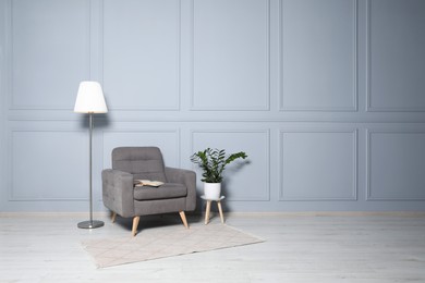 Photo of Cosy armchair, floor lamp and potted plant near light grey wall in room, space for text. Interior design