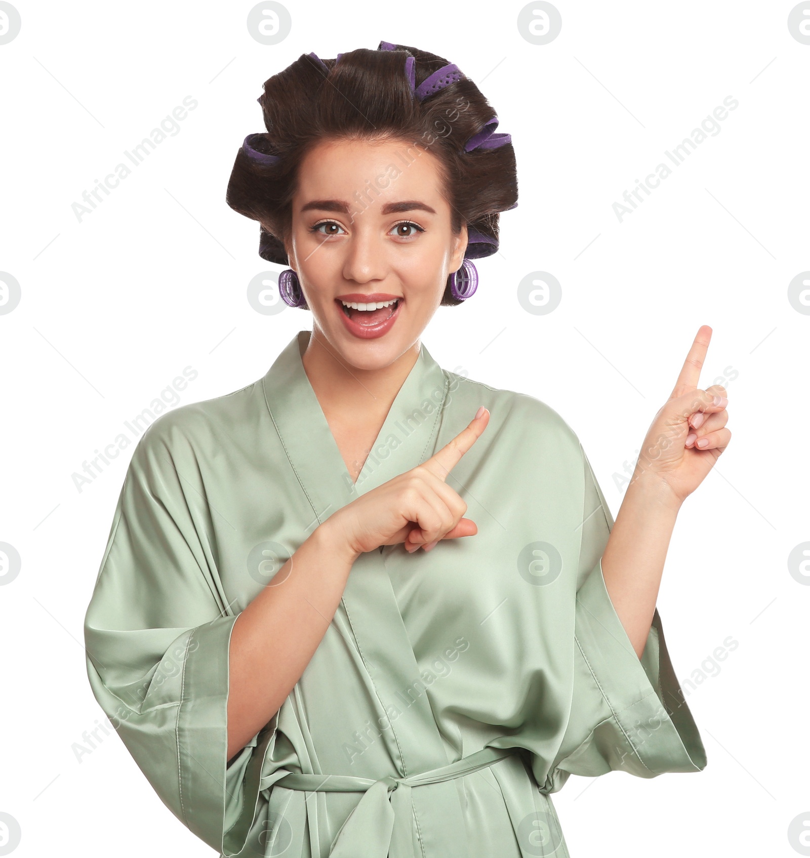 Photo of Happy young woman in silk bathrobe with hair curlers on white background