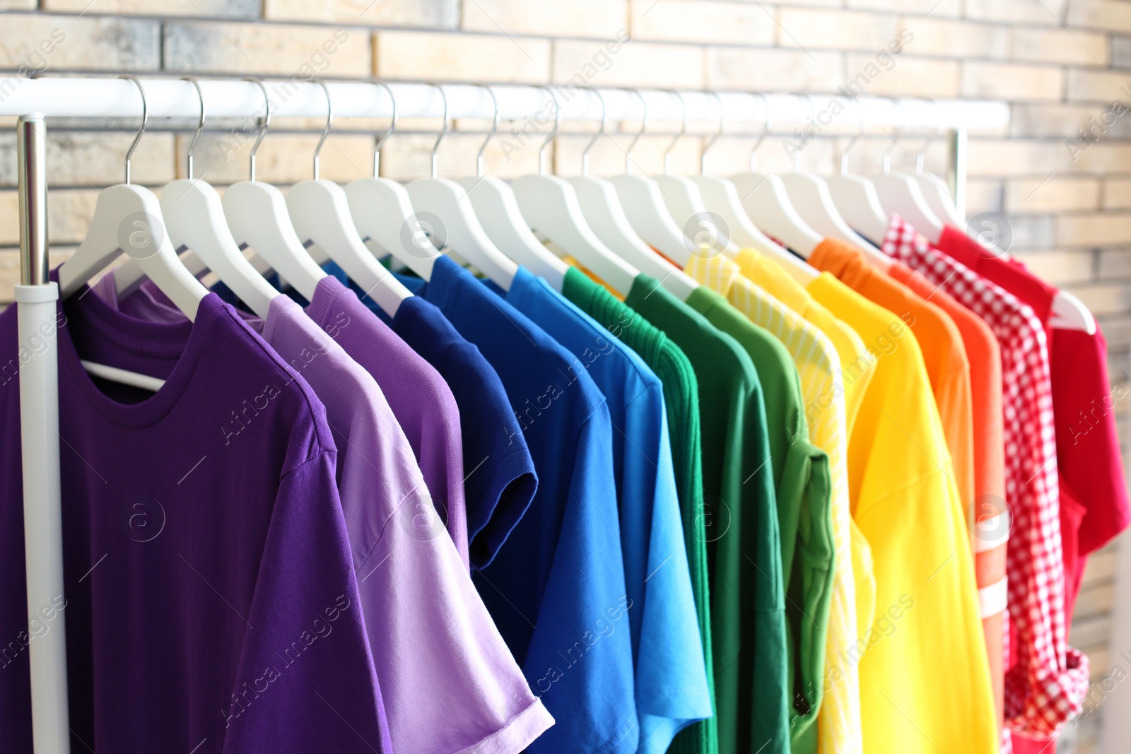 Photo of Rack with rainbow clothes on brick wall background