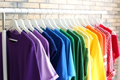 Photo of Rack with rainbow clothes on brick wall background