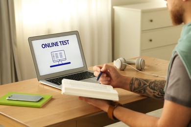 Man taking online test on laptop at desk indoors, closeup