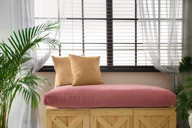 Photo of Bench made of wooden crates and pillows near window in room. Interior design