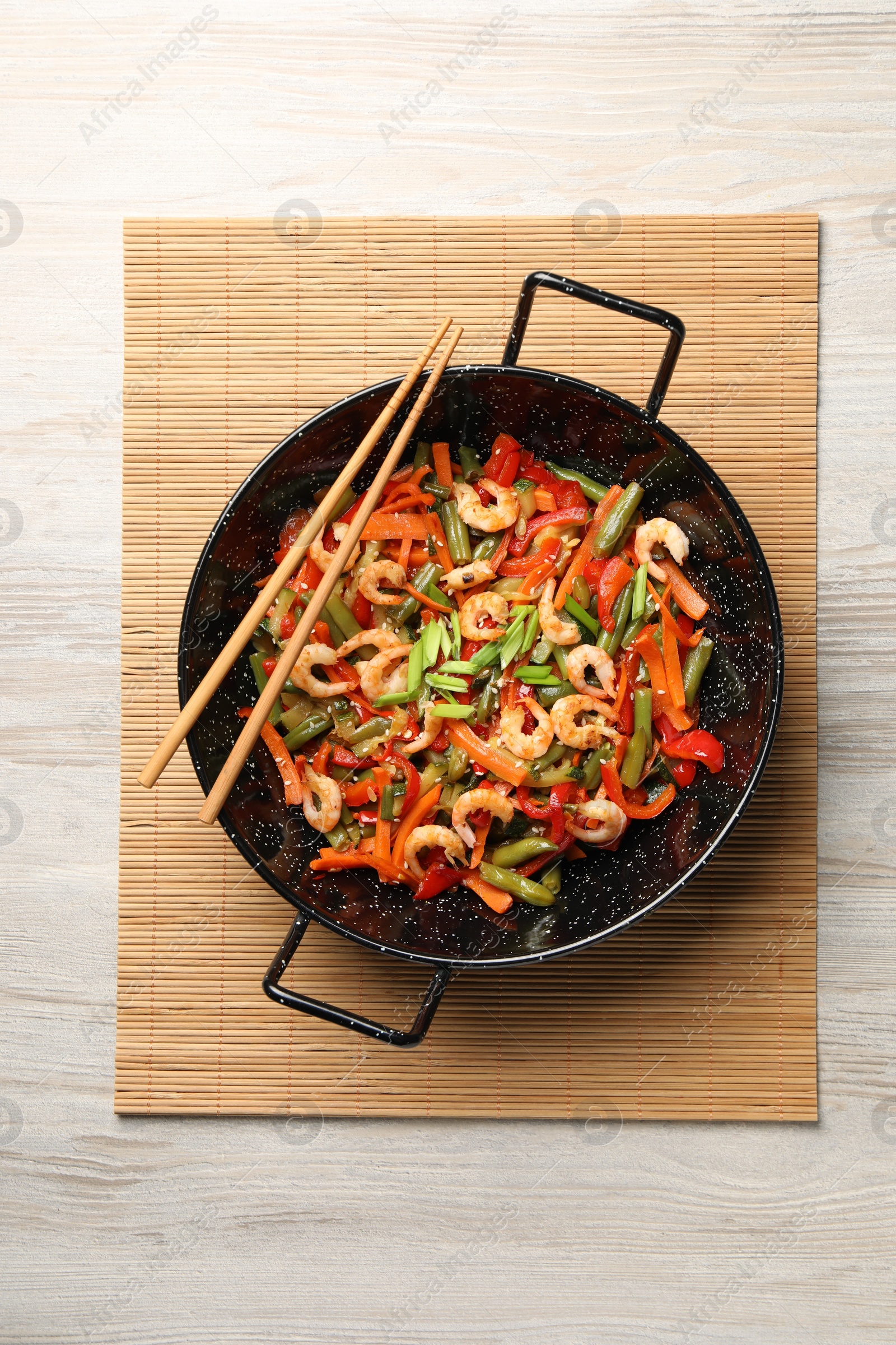 Photo of Shrimp stir fry with vegetables in wok and chopsticks on wooden table, top view